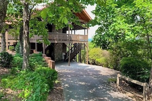 Eine Holzhütte mit einem Balkon, umgeben von Bäumen und einem Kiesweg.