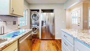 Une cuisine équipée d’un réfrigérateur en acier inoxydable, d’un lave-linge et d’un sèche-linge intégrés, et d’un plan de travail en marbre.
