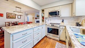 Une cuisine moderne avec des meubles blancs, un plan de travail en granit, des appareils électroménagers en acier inoxydable et un coin repas avec des chaises en bois.