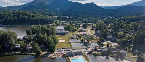 Vista aérea de um resort à beira de um lago, com piscina, quadras de tênis e um clube.