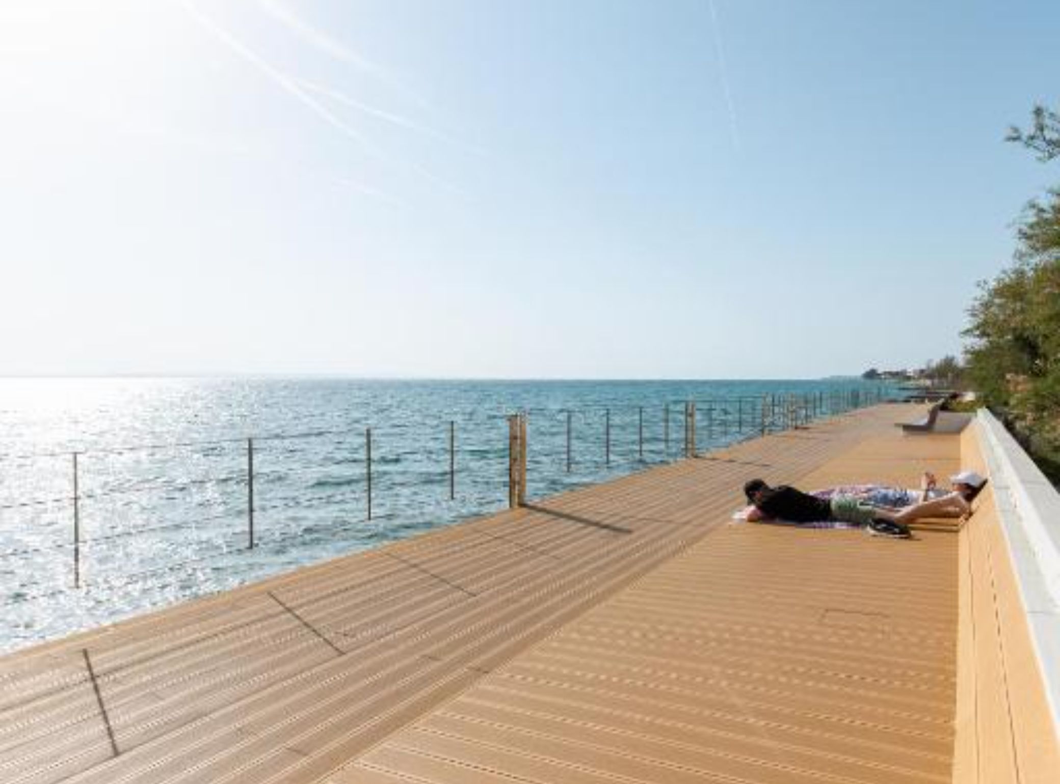 Una terraza de madera con barandilla, con vista a un mar tranquilo.