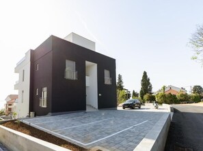 Ein modernes, zweistöckiges Gebäude mit flachem Dach, Auffahrt und geparktem Auto.