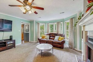 A living room with a ceiling fan, a fireplace, a leather sofa, and a television. - Charming Riverfront House with Full Kitchen, Wifi, and Central AC | Dog-Friendly (Marshall)
