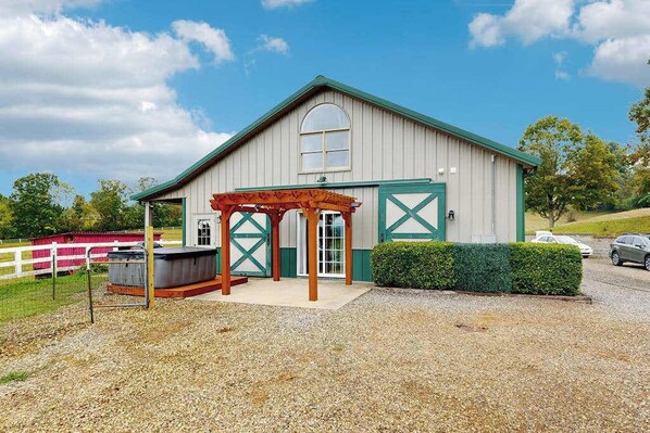 A barn with a covered outdoor area, a hot tub, and a gravel driveway.