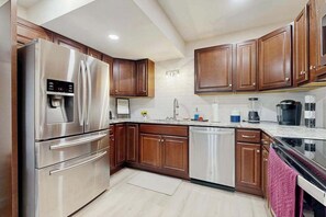 A modern kitchen with stainless steel appliances, wooden cabinets, and a white countertop.