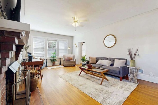 Ein großzügiges Wohnzimmer mit Holzböden, einem grauen Sofa, einem Couchtisch und einem Kamin.