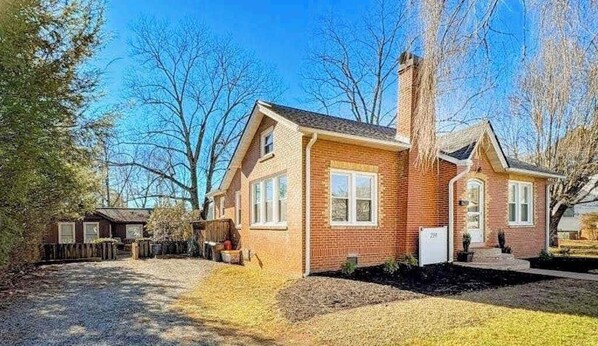 A single-story brick house with a chimney, a front yard, and a wooden fence. - Centrally located home, with cottage, in Brevard - close to outdoor activities! (Brevard)