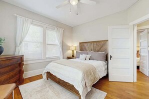 Ein Schlafzimmer mit einem hölzernen Bett, weißen Vorhängen, einem Deckenventilator und einem Nachttisch mit Lampe.