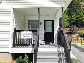 Ein weißes Gebäude mit einer Veranda, einem Schild mit der Aufschrift 'Gap Creek Cottage' und einer schwarzen Tür.