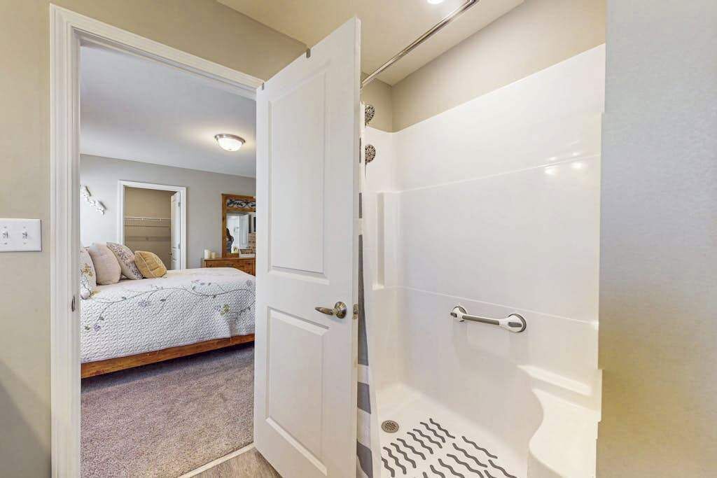 A bedroom with a bed, a door leading to a bathroom with a shower.