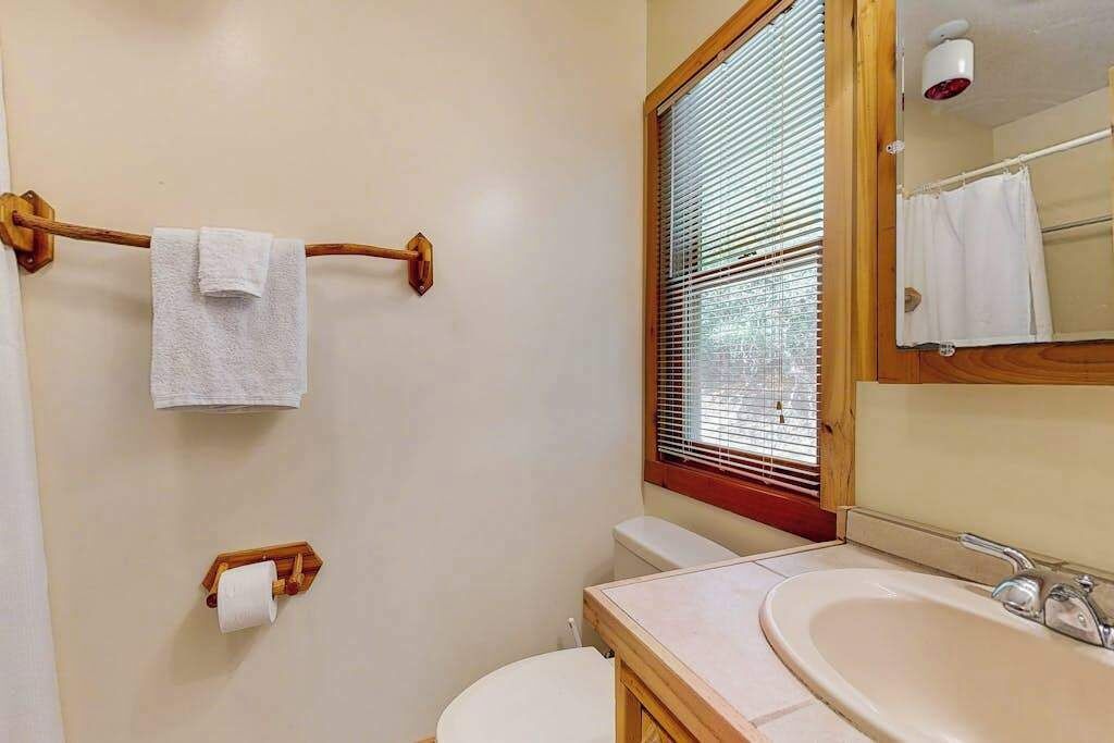 A bathroom with a toilet, sink, wooden towel rack, and a window with blinds.