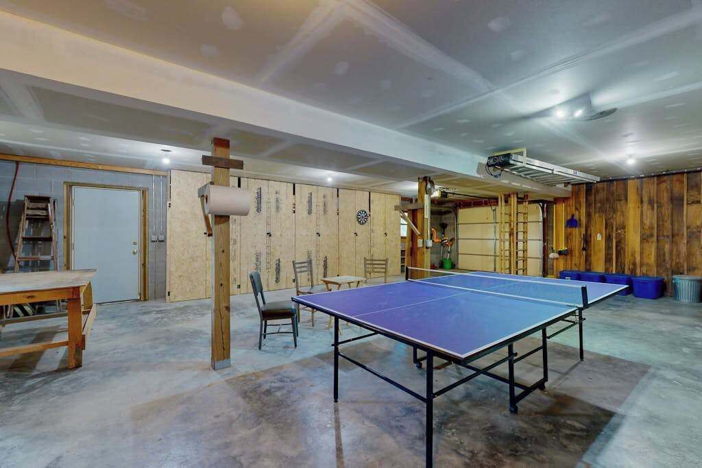 A ping pong table in a room with wooden walls, a ceiling fan, and a ladder.