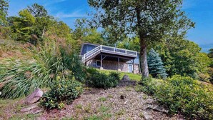 Une maison en pierre dotée d’un balcon, entourée d’une végétation luxuriante et d’arbres.