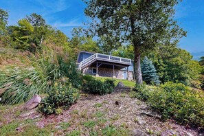 A stone house with a balcony, surrounded by lush greenery and trees. - Charming 2 BR home with Stunning Views from outdoor deck (Penrose)