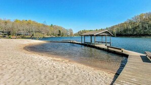 A sandy beach with a wooden dock leading to a covered pavilion by a calm lake, surrounded by trees. - Charming house in Brevard with heated outdoor pool, tennis court, and a gym (Brevard)