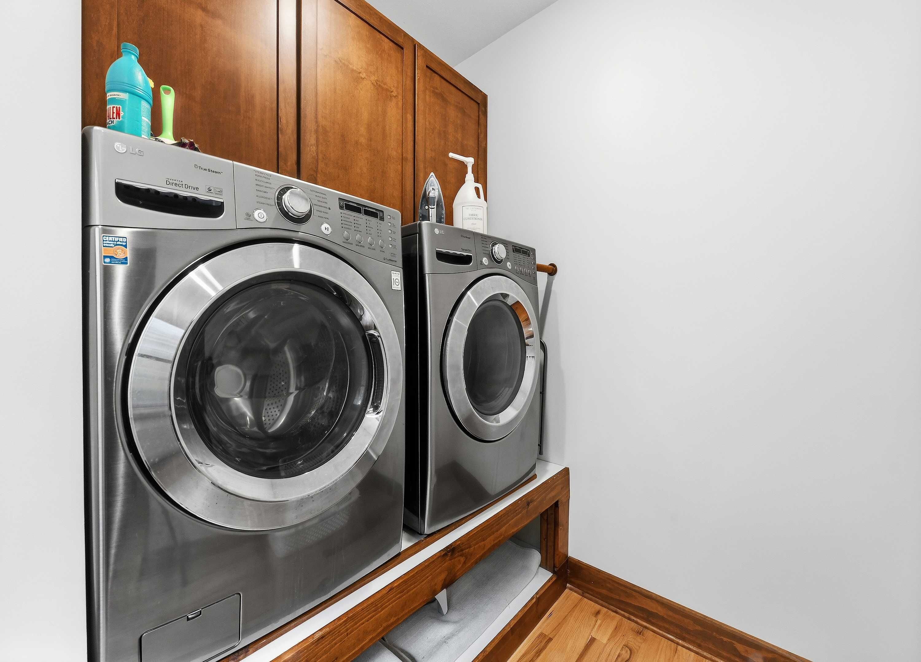 A laundry room with two front-loading washing machines, wooden cabinets, and a wooden floor.