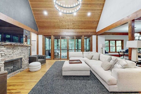 A spacious living room with a stone fireplace, a large sectional sofa, and a wooden ceiling. - Charming house in Brevard with heated outdoor pool, tennis court, and a gym (Brevard)