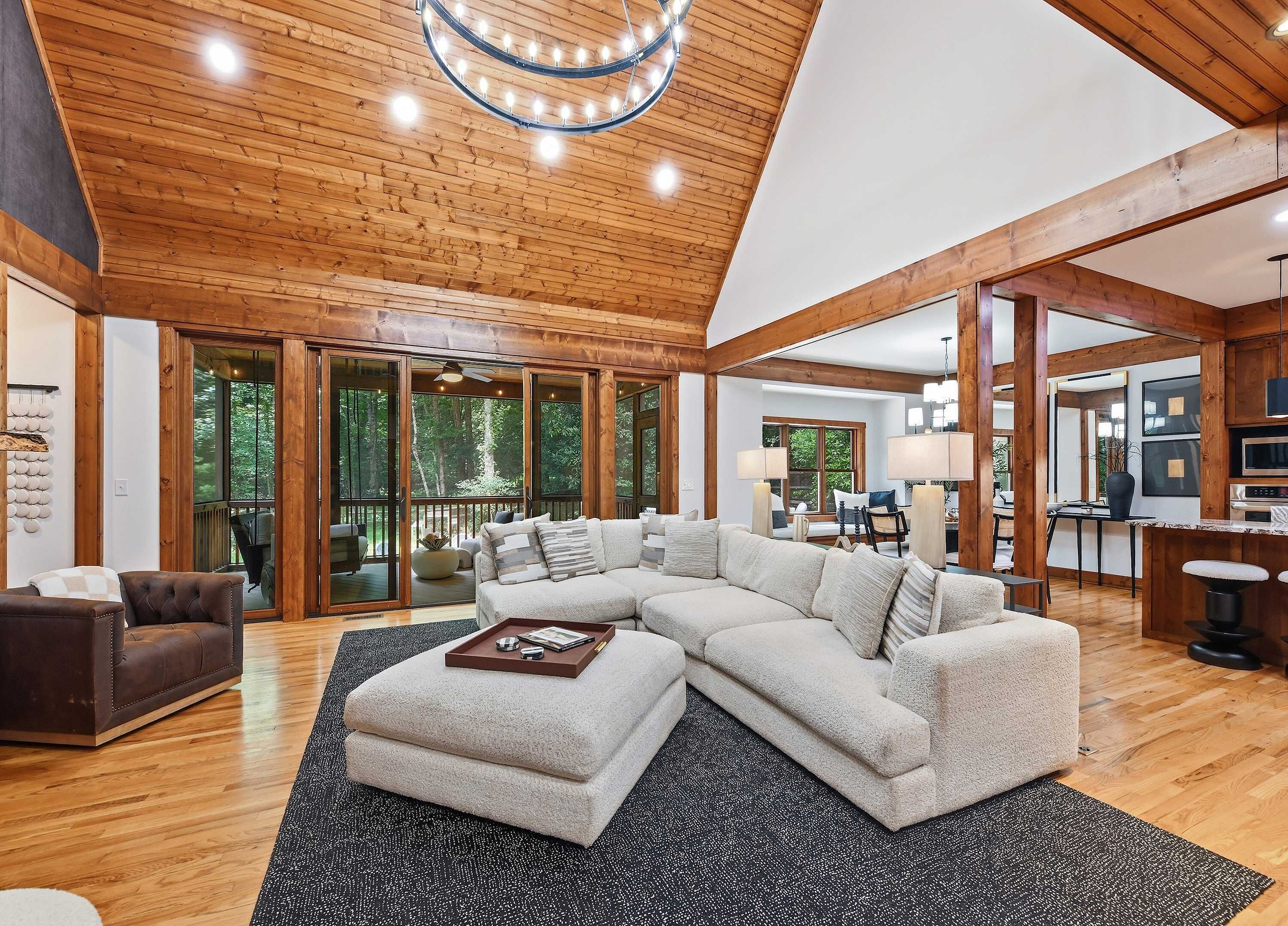 A spacious living room with a large sectional sofa, a wooden ceiling, and a view of the outdoors through large sliding glass doors.