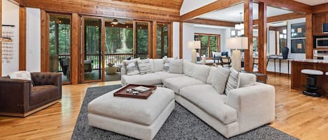A spacious living room with a large sectional sofa, a wooden ceiling, and a view of the outdoors through large sliding glass doors.