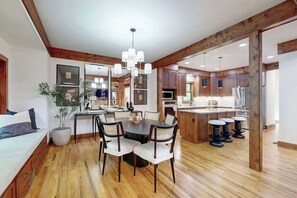 A modern kitchen with wooden beams, a dining area with a chandelier, and a large island with bar stools. - Charming house in Brevard with heated outdoor pool, tennis court, and a gym (Brevard)