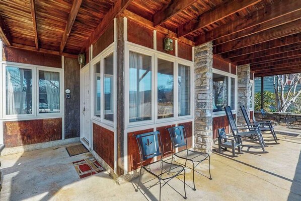 A covered patio with wooden beams, stone pillars, and a seating area with chairs. - Morris Villa Lower (Lake Junaluska)