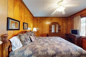 A wooden-paneled room with a bed, a television, a mirror, and framed pictures on the wall. - Morris Villa Lower (Lake Junaluska)