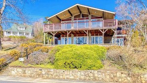 Um edifício de dois andares com varanda, parede de pedra e vegetação ao redor.