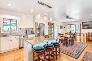 A spacious kitchen with a large island, bar stools, and a dining area with a wooden table and chairs. - Armstrong House upper level (Lake Junaluska)