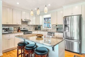 A modern kitchen with white cabinets, stainless steel appliances, a marble island, and bar stools. - Armstrong House upper level (Lake Junaluska)