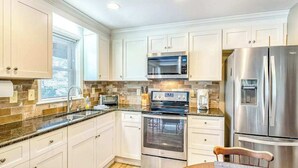 A modern kitchen with white cabinets, stainless steel appliances, and a window providing natural light. - Armstrong Apartment (Lake Junaluska)