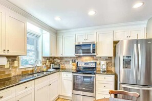A modern kitchen with white cabinets, stainless steel appliances, and a window providing natural light. - Armstrong Apartment (Lake Junaluska)