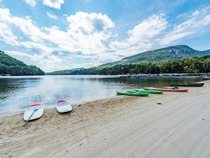 A beach with kayaks lined up on the sand, a calm lake, and a forested hill in the background. - Family Escape at Rumbling Bald with Firepit, Games & Fiber Internet (Lake Lure)