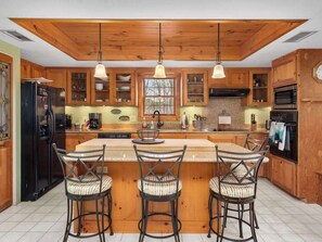 A kitchen with wooden cabinets, a central island with bar stools, pendant lights, and a black refrigerator. - Family Escape at Rumbling Bald with Firepit, Games & Fiber Internet (Lake Lure)