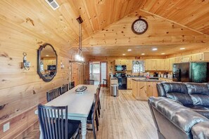 Ein Holzinterieur mit einem Esstisch, Stühlen, einer Couch, einer Küchenzeile und einer Uhr an der Wand.