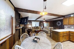 Eine rustikale Küche mit Holzausbau, einem Esstisch mit Stühlen, einem an der Wand montierten Fernseher und einem Deckenventilator.