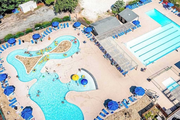 Une piscine avec plusieurs couloirs de nage, une pataugeoire séparée et des espaces de détente avec des parasols.