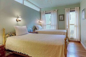 A bedroom with two beds, a nightstand, a lamp, and a window with curtains. - Friday Cottage (Lake Junaluska)