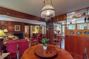A wooden-finished room with a chandelier, a fireplace, and a dining area with a round table. - Friday Cottage (Lake Junaluska)