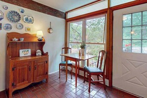 A dining area with a wooden table and chairs, a cabinet with decorative plates, and a window with a view of trees. - Friday Cottage (Lake Junaluska)