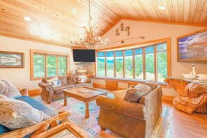 Ein geräumiges Wohnzimmer mit großem Fenster, einer Kristallleuchtre und einem Fernseher.