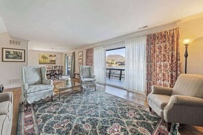 Ein geräumiges Wohnzimmer mit großem Fenster, zwei Sesseln, einem Couchtisch und einem gemusterten Teppich.