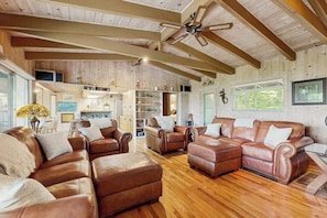 Ein geräumiges Wohnzimmer mit Ledersofas, Holzböden und Deckenventilator.