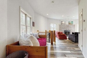 A room with a wooden bed, a red sofa, a grey sofa, a fireplace, and a brick wall. - Bright Brevard House w/ Fireplaces, Jetted Tub, Fire Pit & Bike Storage (Brevard)