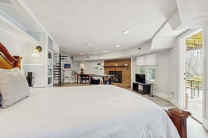 A bedroom with a large bed, a fireplace, a desk, and a view of the outdoors. - Bright Brevard House w/ Fireplaces, Jetted Tub, Fire Pit & Bike Storage (Brevard)