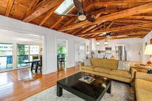 Ein geräumiger Wohnbereich mit Holzboden, einer Couch, einem Couchtisch und einer Küche im Hintergrund.