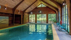 Una piscina interior con vigas de madera, ventanas amplias y una silla para socorrista.