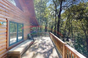 Una cabaña de madera con terraza, ventanas grandes y vistas a un bosque.