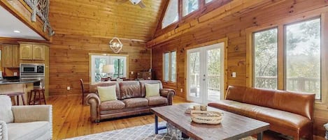 Un interior de cabaña amplio con paredes de madera, una gran mesa de comedor, sofás de cuero y una zona de cocina.