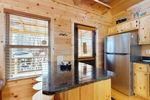 Ein Interieur einer Holzhütte mit Küchenbereich, darunter ein Edelstahlkühlschrank, Holzschränke und eine Arbeitsplatte aus Granit.