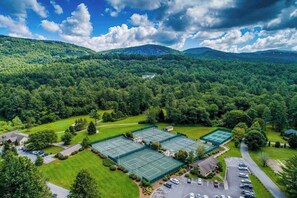 An aerial view of a property with multiple tennis courts, surrounded by lush greenery and mountains. - Mountain-view condo with pools, hot tub, sauna, tennis, game room, & balcony (Sapphire)